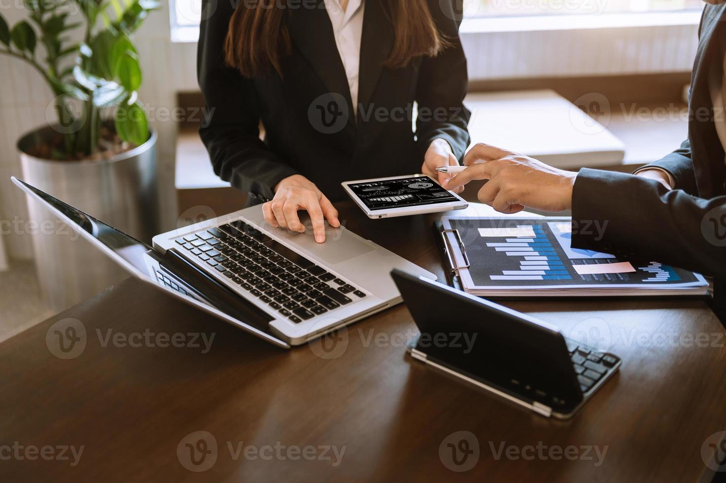 Documentos comerciales en el escritorio de la oficina con tableta, gráfico y dos colegas discutiendo el trabajo de datos foto