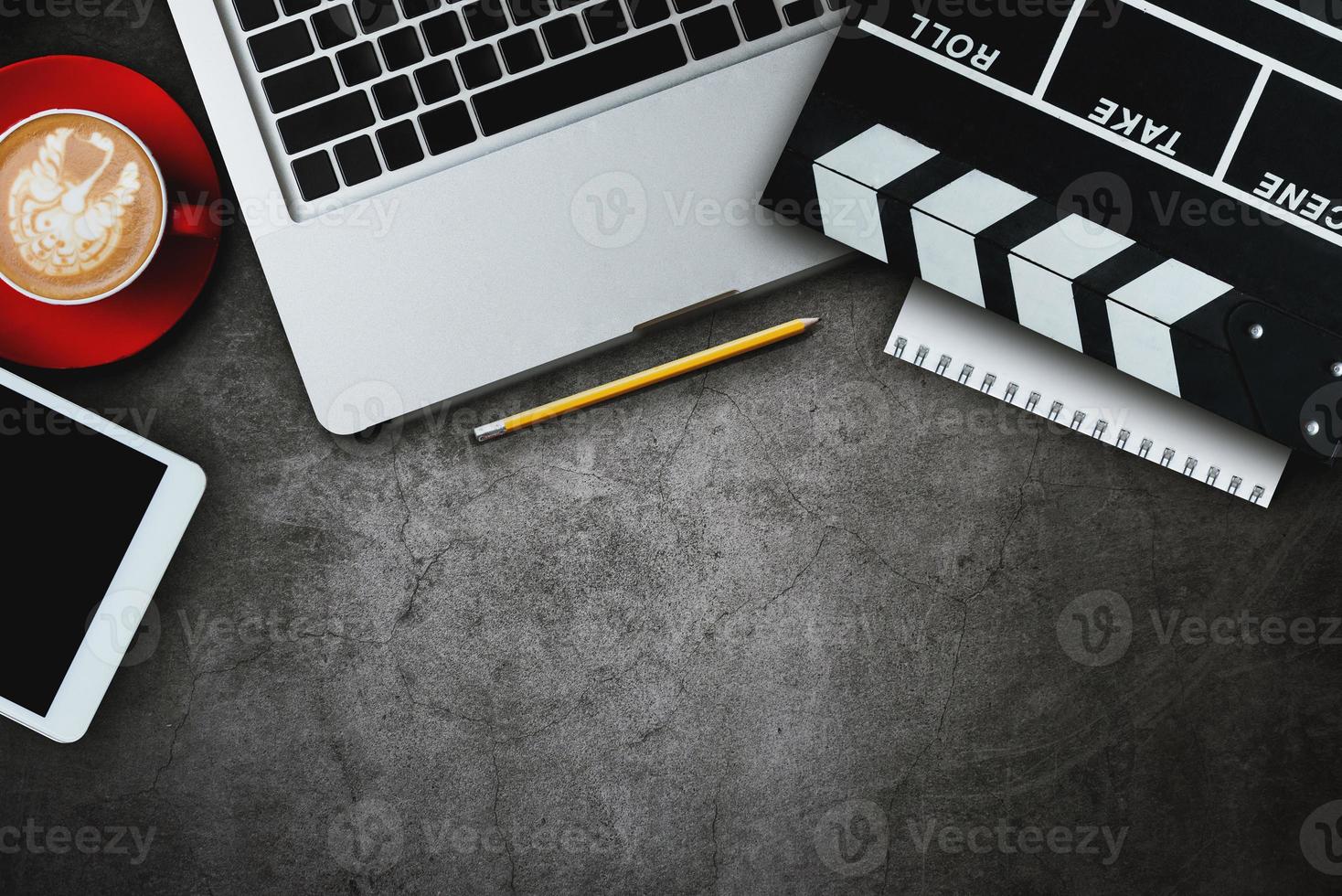 office stuff with Movie clapper, laptop, smartphone, tablet, coffee cup, pen, notepad and documents on the wood table top view shot. photo