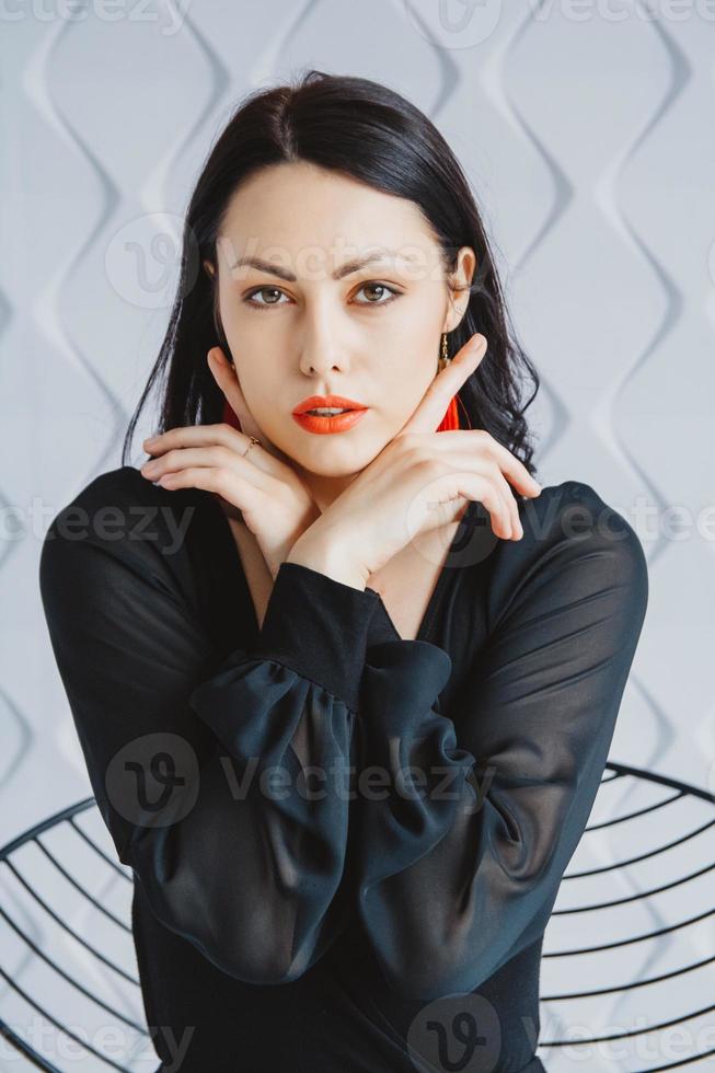 Fashion portrait of a stylish brunette woman wearing a black dress. Woman with long hair wearing red earrings. Posing in studio. Place for text or advertising photo