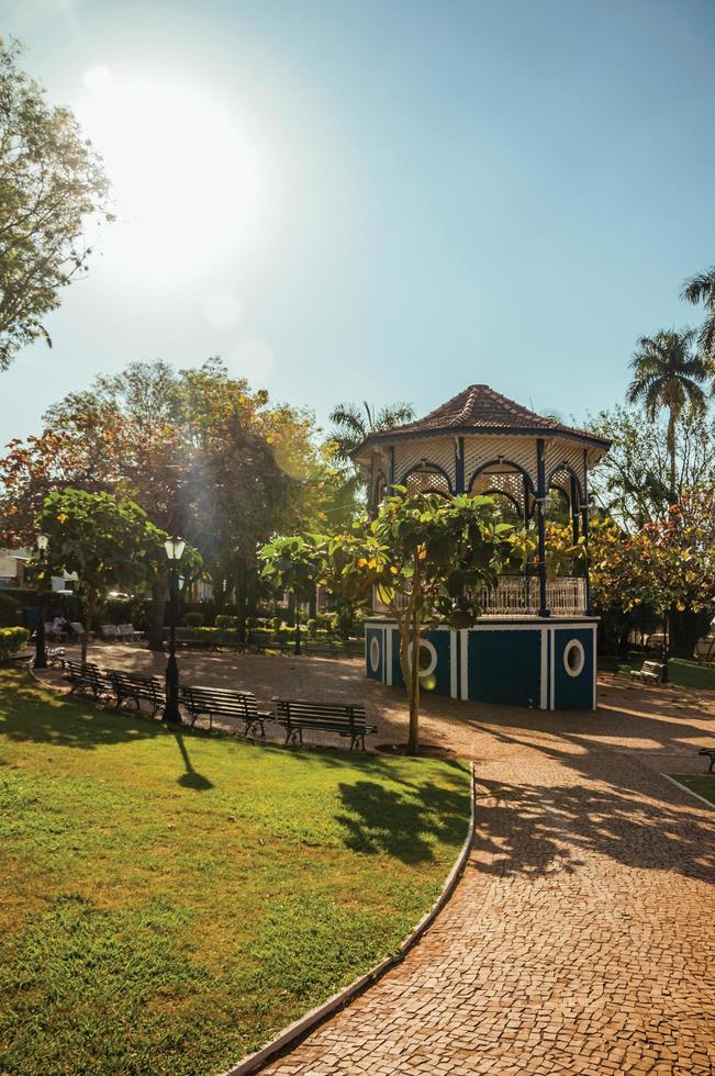 Old and colorful gazebo of square in the middle of verdant garden full of trees, in a bright sunny day at Sao Manuel. A cute little town in the countryside of Sao Paulo State. Brazil. photo