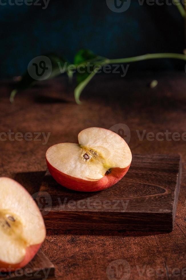 The apples on the plate look like oil paintings under the dim light on the wood grain table photo