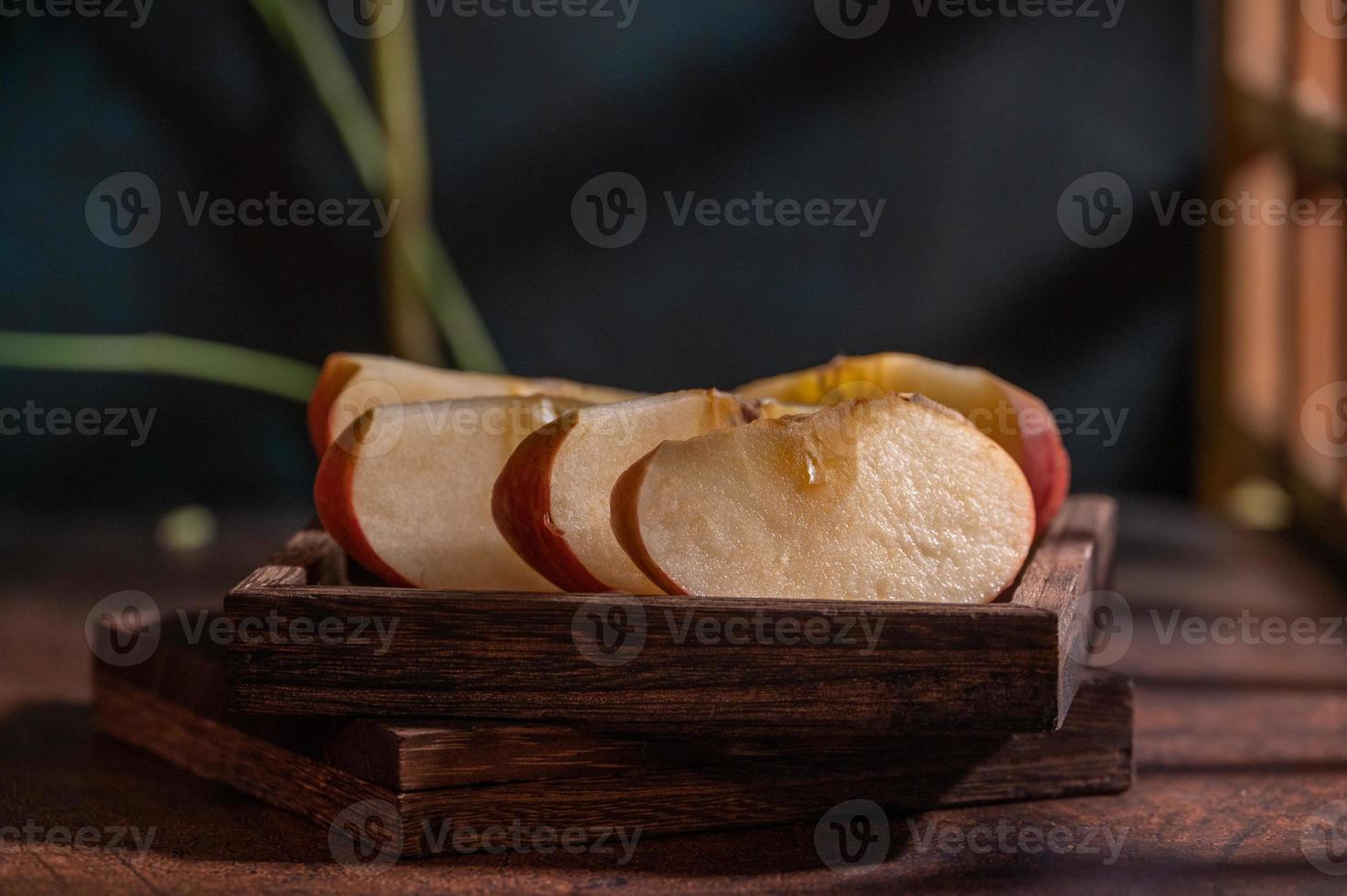 The apples on the plate look like oil paintings under the dim light on the wood grain table photo