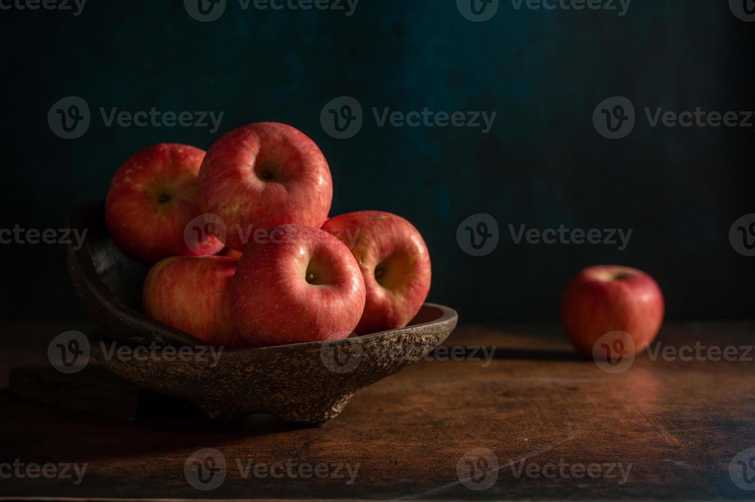 The apples on the plate look like oil paintings under the dim light on the wood grain table photo