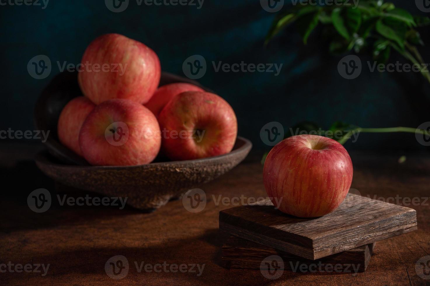 The apples on the plate look like oil paintings under the dim light on the wood grain table photo