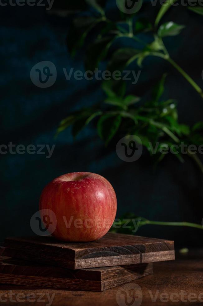 The apples on the plate look like oil paintings under the dim light on the wood grain table photo