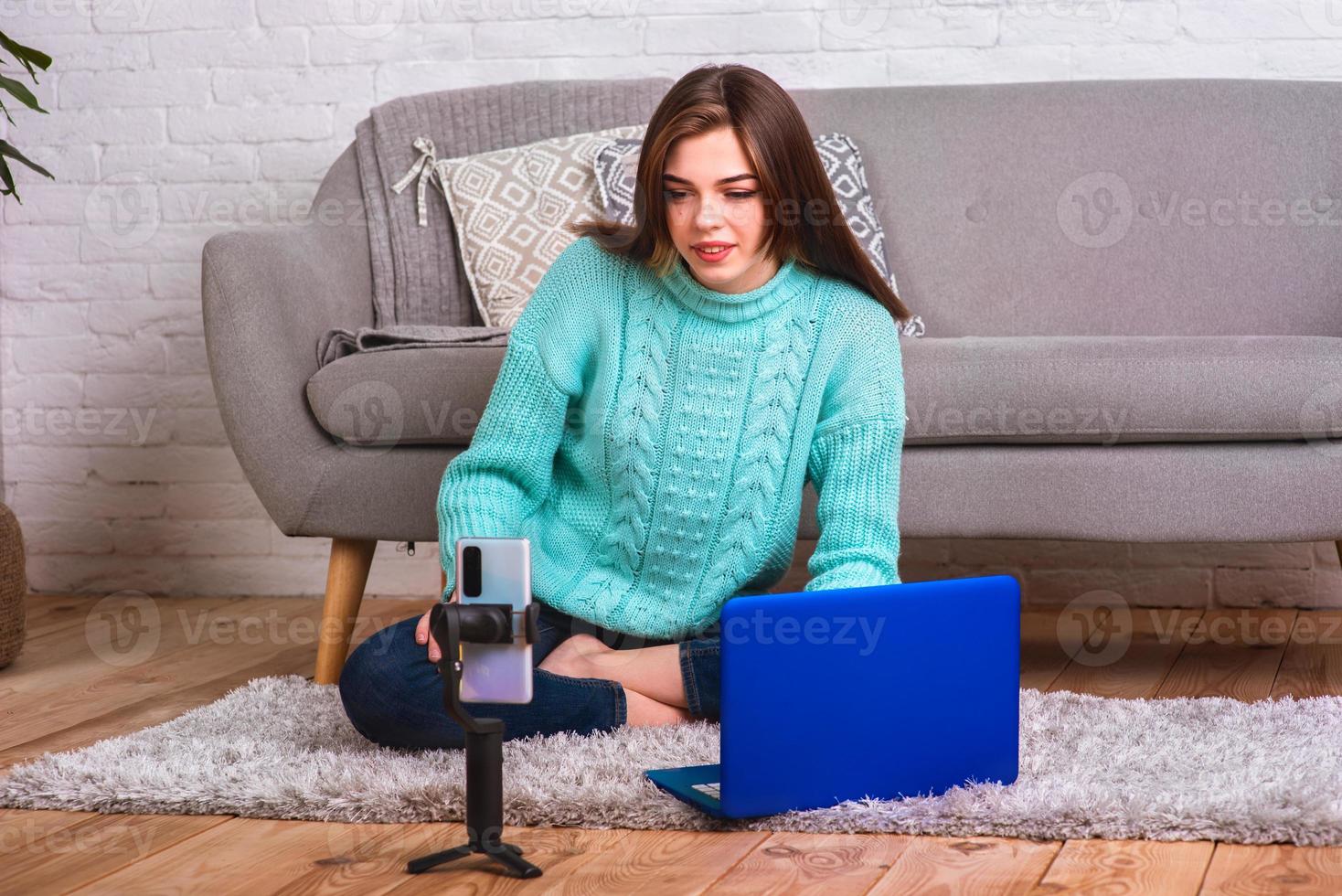 A beautiful, young girl communicates with friends in an online conference using a phone and a laptop. Quarantine Distance Learning photo