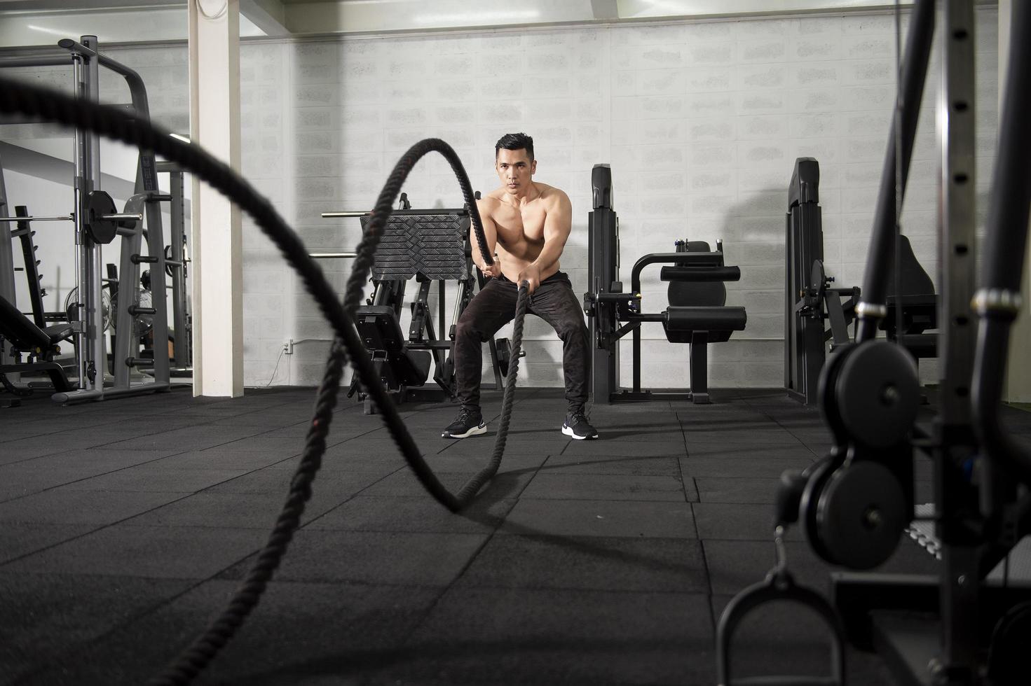 Asian athletic man with  rope doing exercise in fitness gym photo