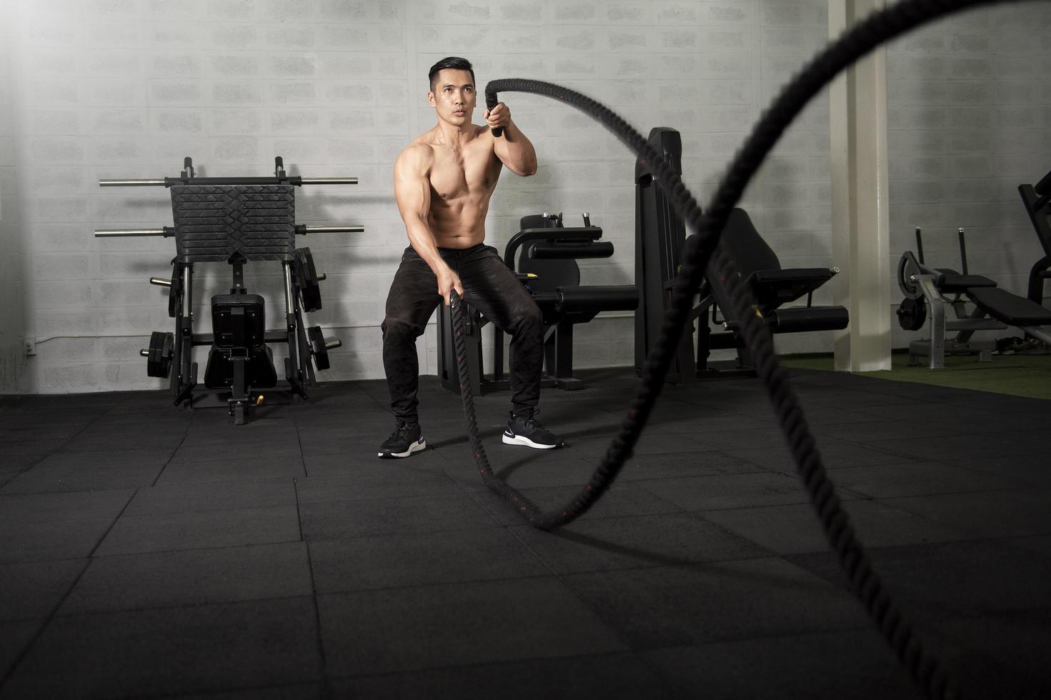 Asian athletic man with  rope doing exercise in fitness gym photo