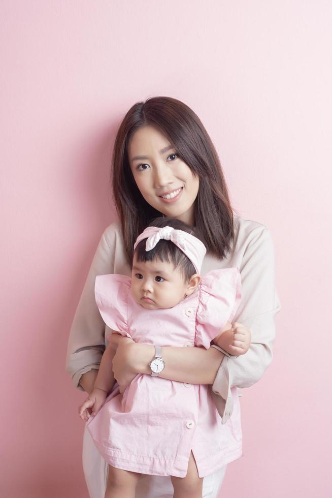 Asian mother and adorable baby girl are happy on pink background photo