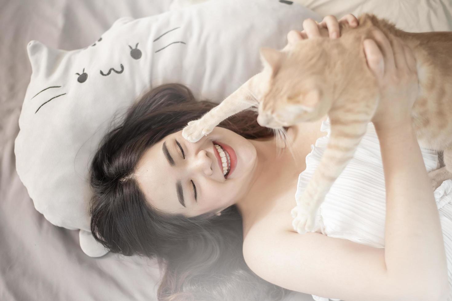 hermosa mujer asiática amante de los gatos está jugando con un gato en su habitación foto