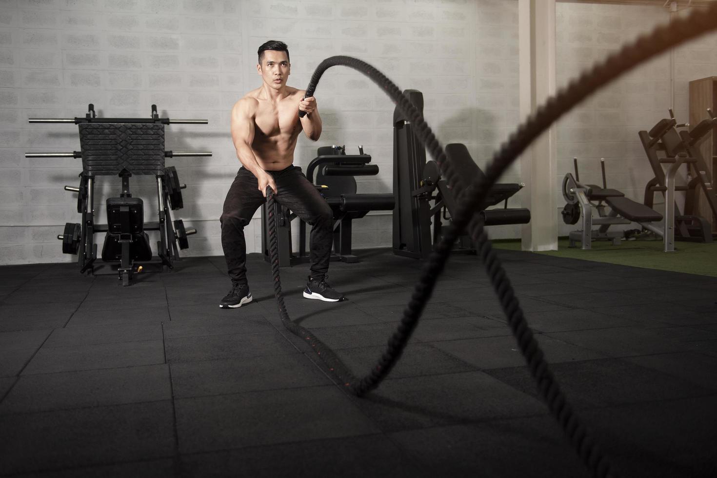 Asian athletic man with  rope doing exercise in fitness gym photo