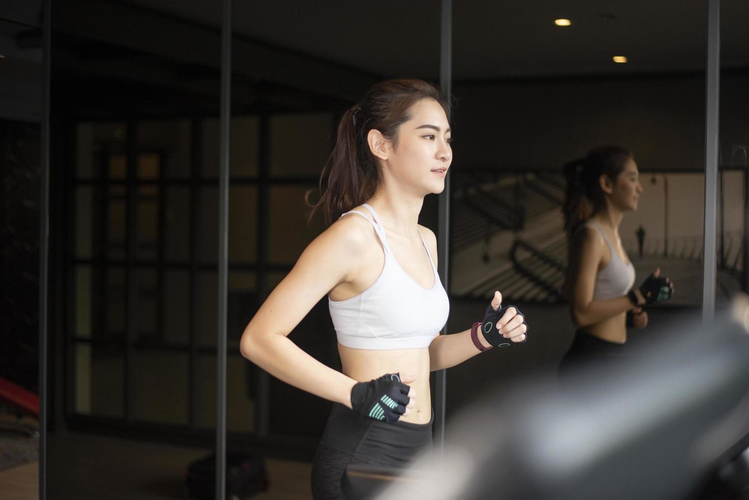 Beautiful asian sport woman is running on treadmill in the gym photo