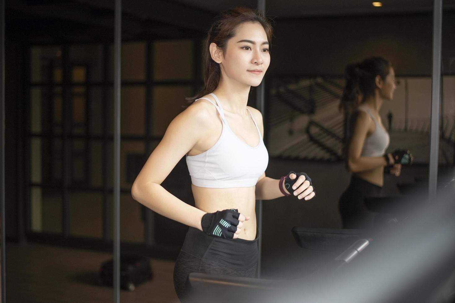 hermosa mujer deportiva asiática está corriendo en la cinta de correr en el gimnasio foto