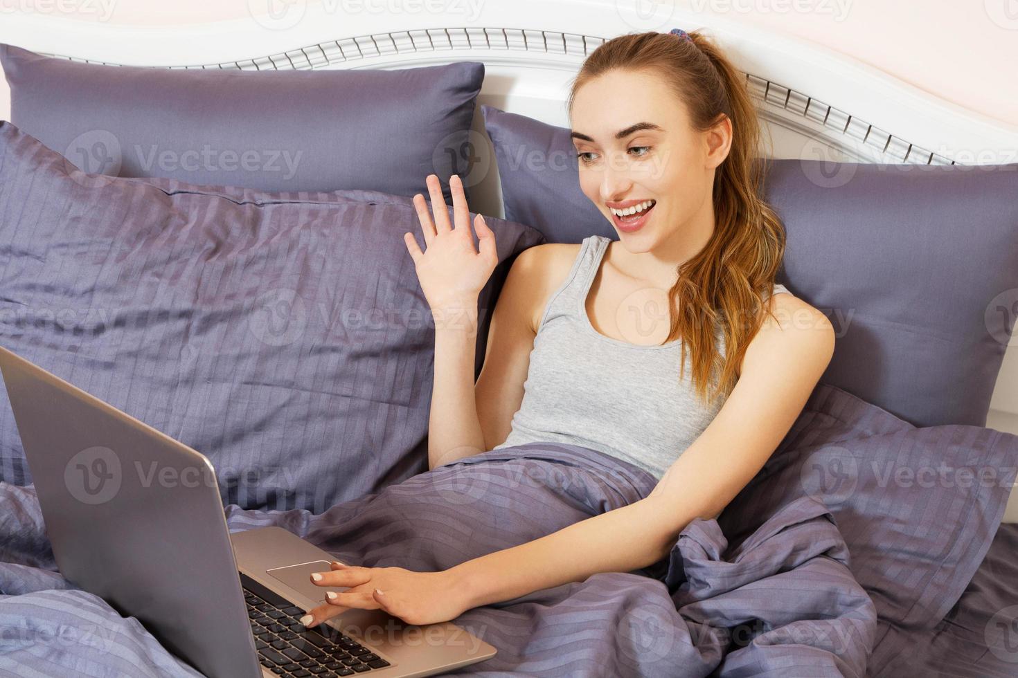 Portrait beautiful smiling young white woman laying in bed relaxing using working on her laptop computer. Positive human face expression emotions customer service satisfaction concept. photo