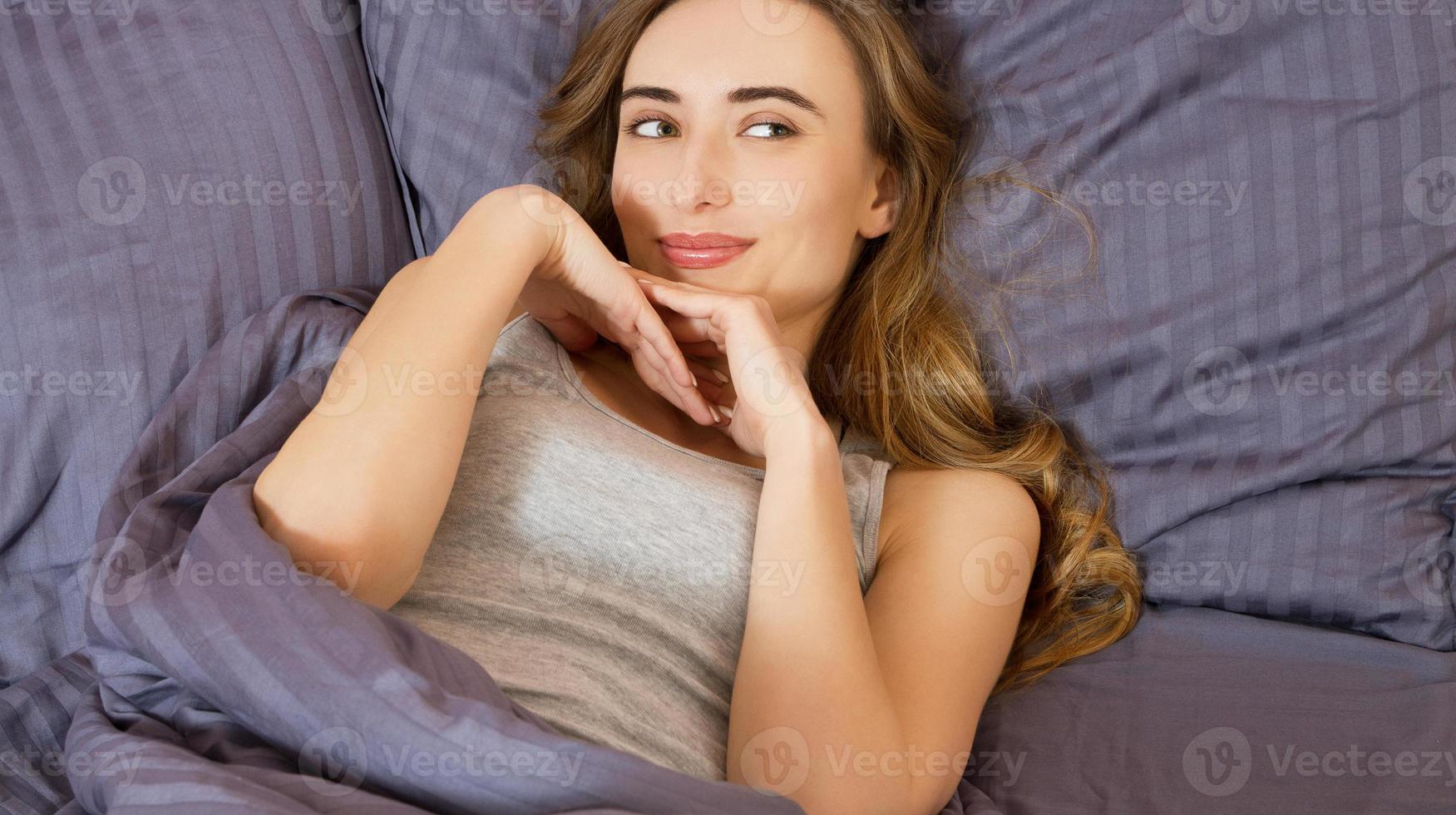 Pretty young beautiful woman on bed in modern apartment smiling after wake up photo