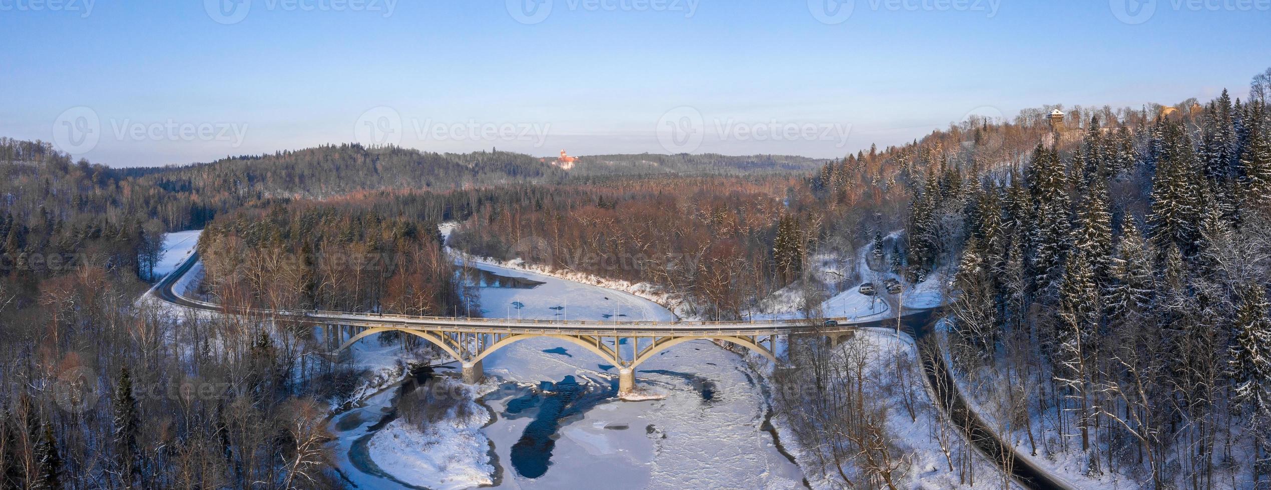 vista aérea del río y del bosque cubierto de nieve después de una ventisca en una neblina matutina. cielo azul claro. las maravillas de invierno. parque nacional de gauja, sigulda, letonia foto