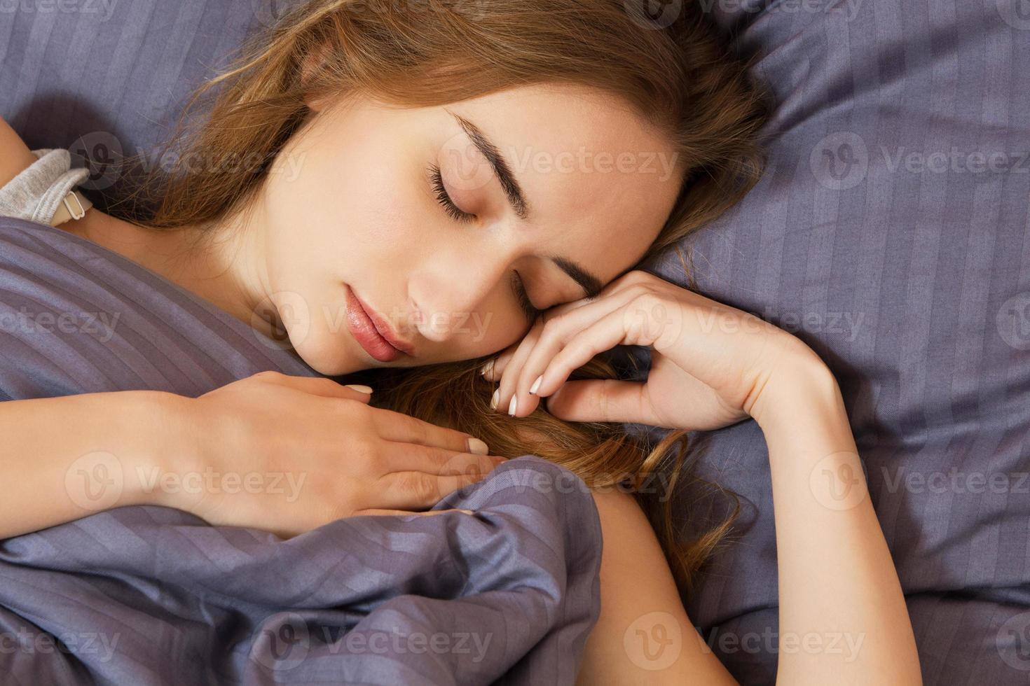 hermosa chica duerme en el dormitorio de cerca, acostada en la cama, aislada foto