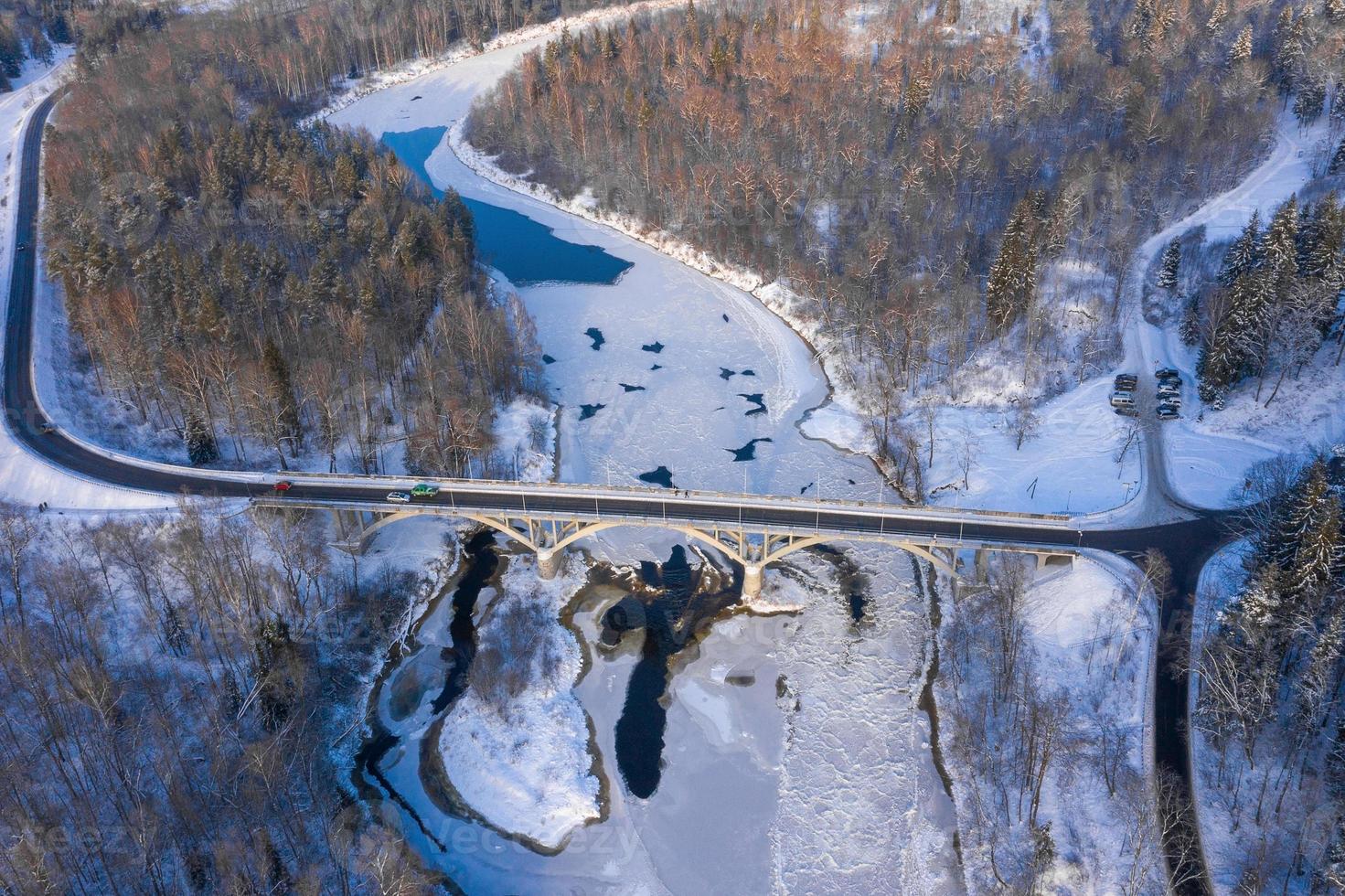 vista aérea de arriba hacia abajo de la temporada de invierno de un puente con una carretera en línea recta sobre el río foto