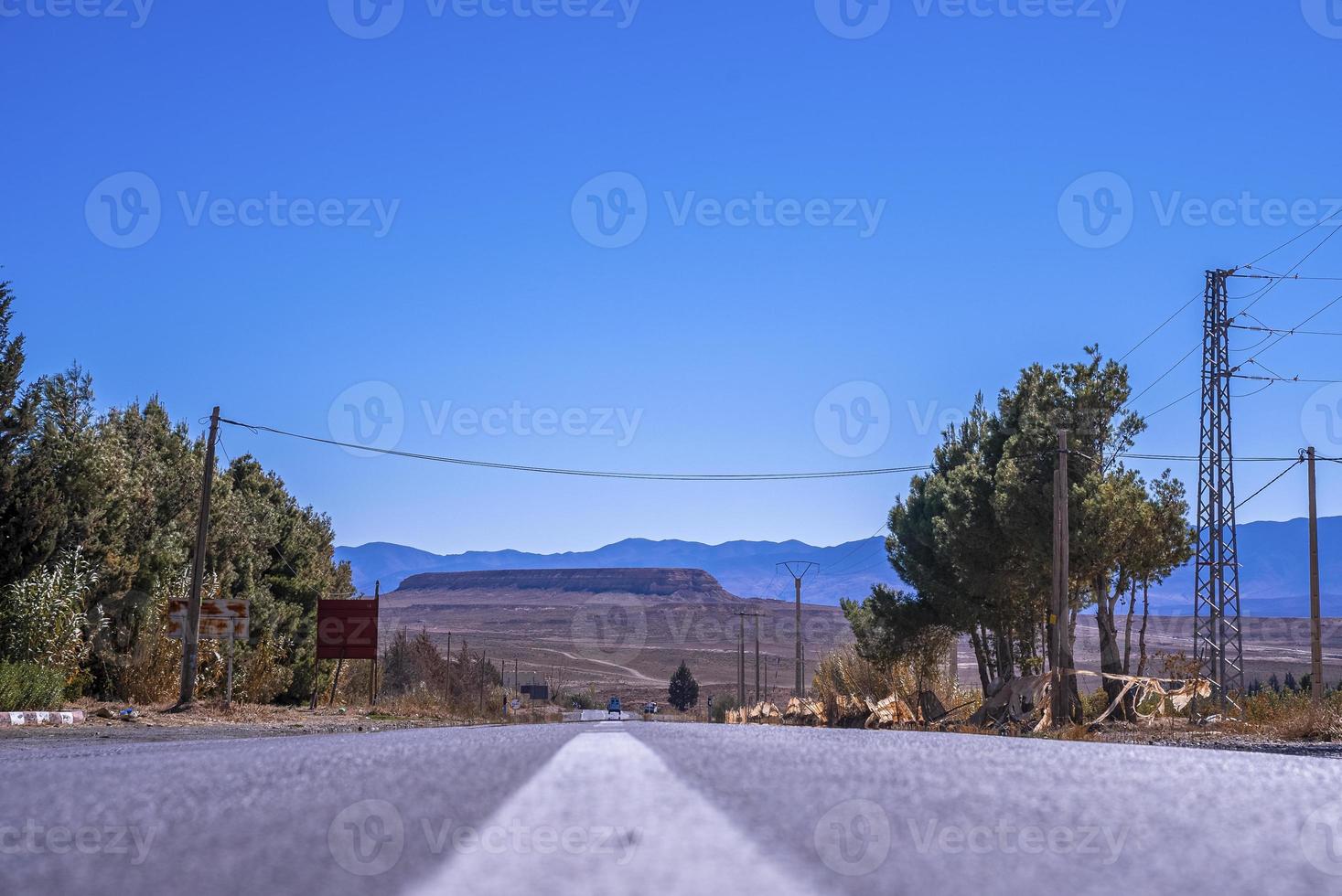 Carretera asfaltada recta con marcas de superficie blanca contra montañas en segundo plano. foto
