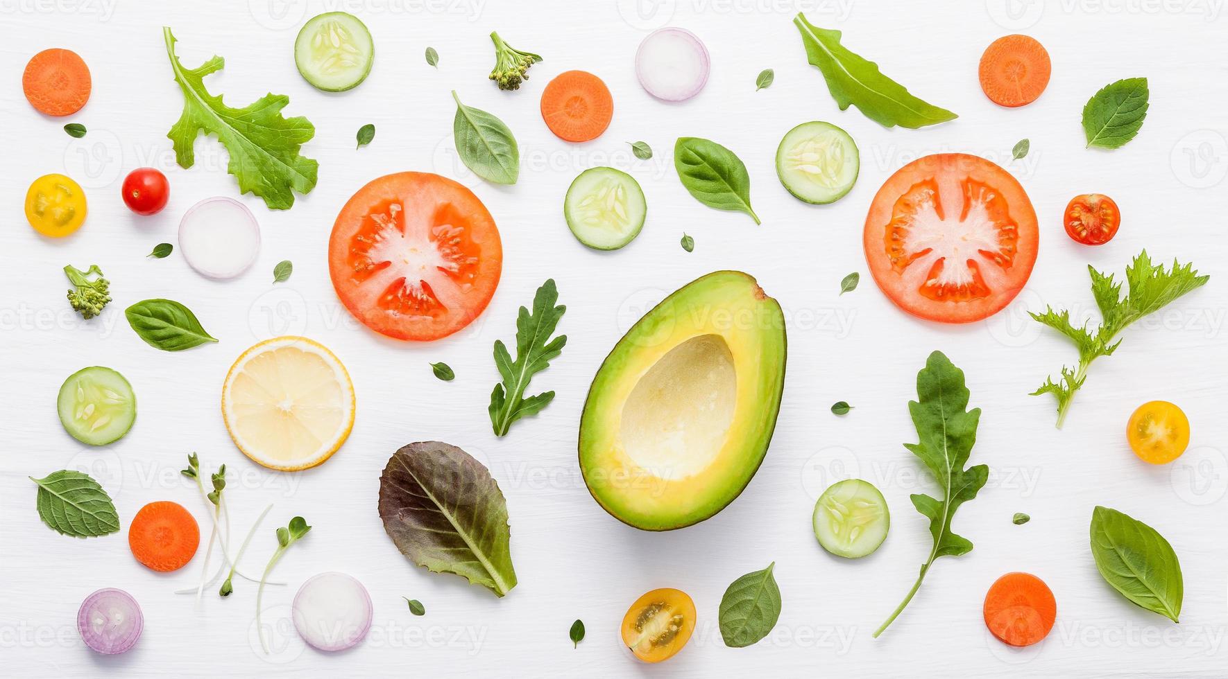 patrón de alimentos con ingredientes crudos de ensalada, hojas de lechuga, pepinos, tomates, zanahorias, brócoli, albahaca, cebolla y limón sobre fondo blanco de madera. foto