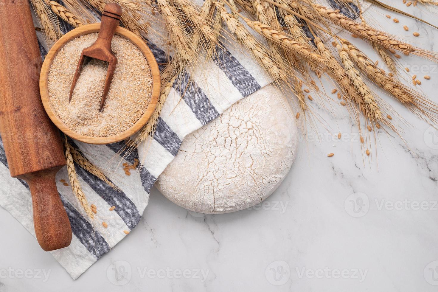 masa de levadura casera fresca descansando sobre una mesa de mármol con espigas de trigo y rodillo. foto