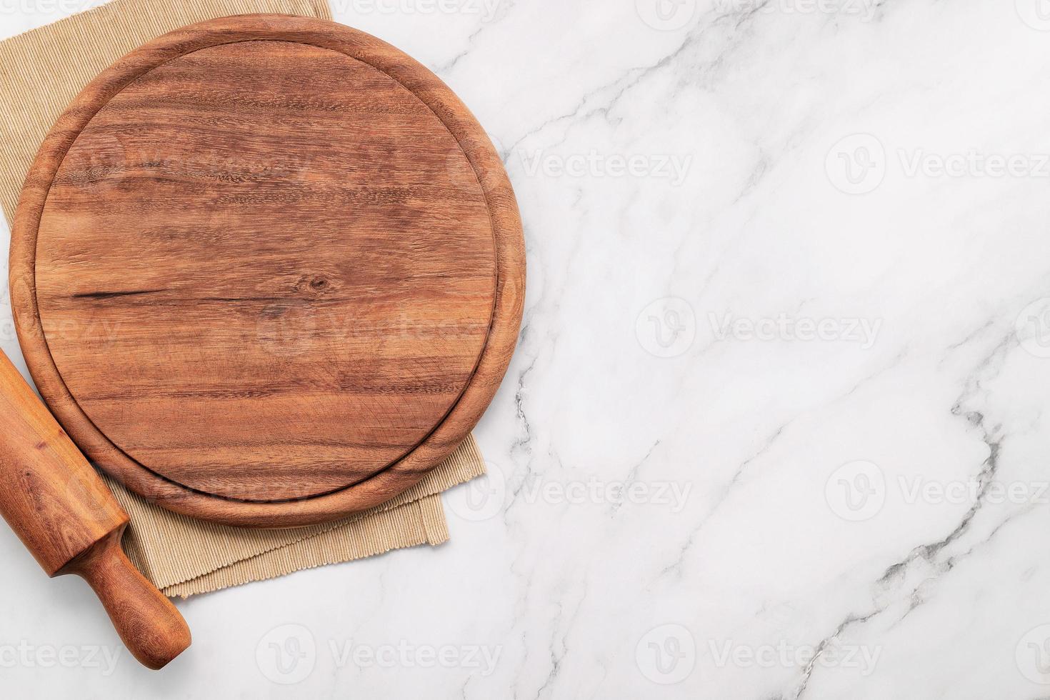 Empty wooden pizza platter with napkin and rolling pin set up on marble stone kitchen table. Pizza board and tablecloth on white marble background. photo
