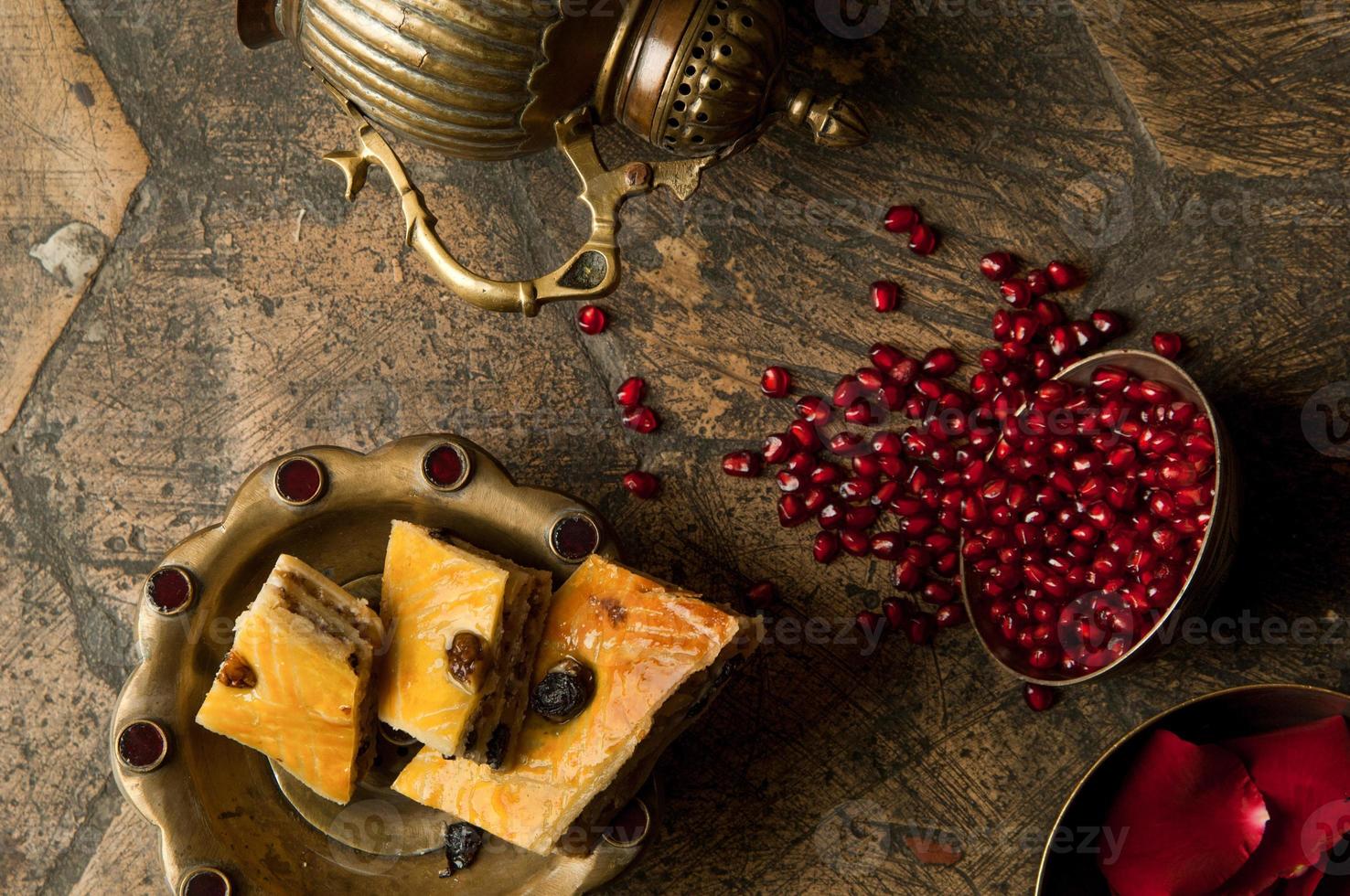 grains and seeds of pomegranate with a copper jug on an old decorative paving stone. an antique copper jug with a pomegranate and cake on an old tile photo
