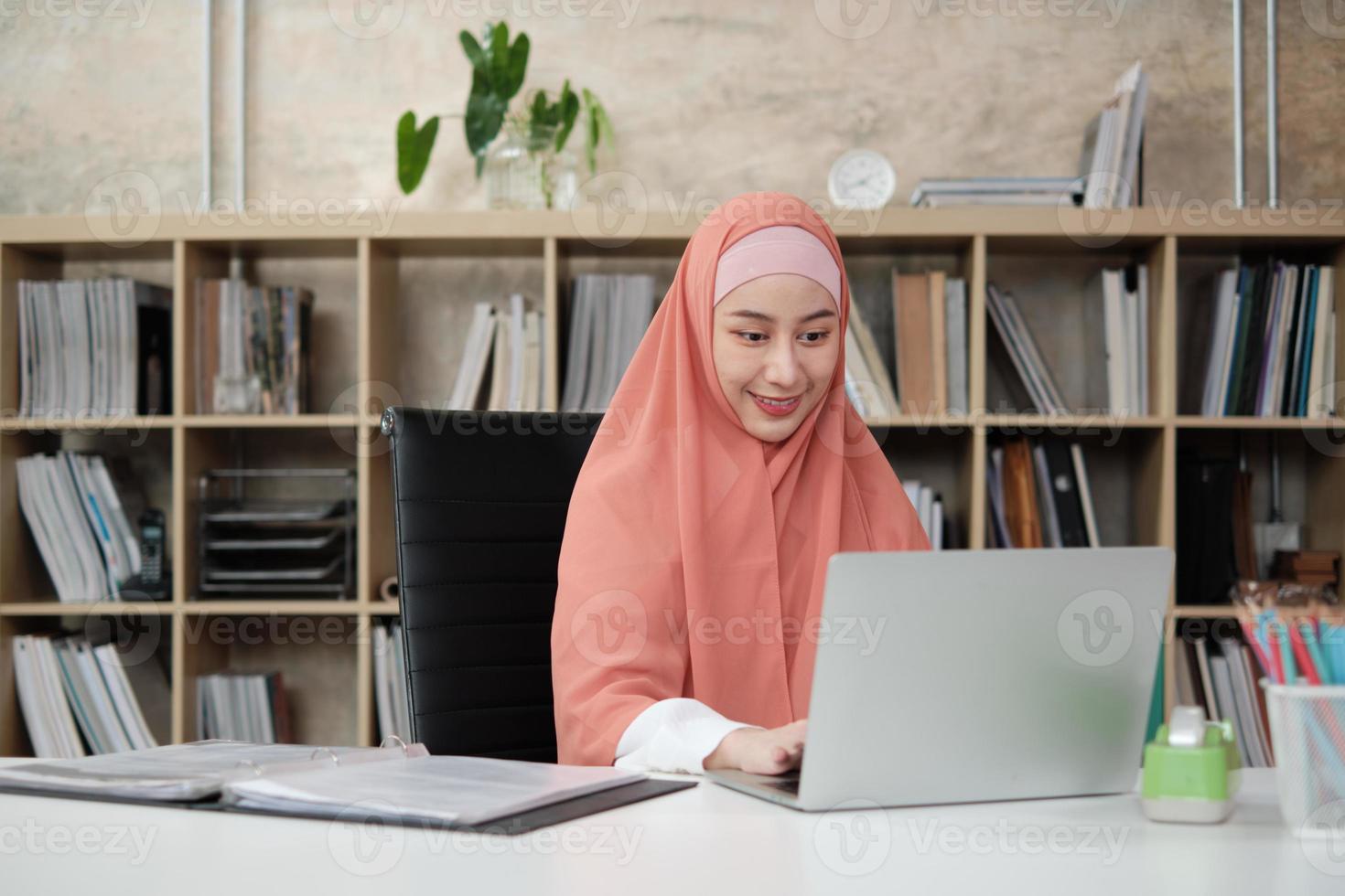 hermosa empresaria de origen étnico asiático trabaja en comercio electrónico usando una computadora portátil, comunicación por Internet en la oficina de la pequeña empresa. persona atractiva, tradicionalmente el islam se viste con hiyab. foto