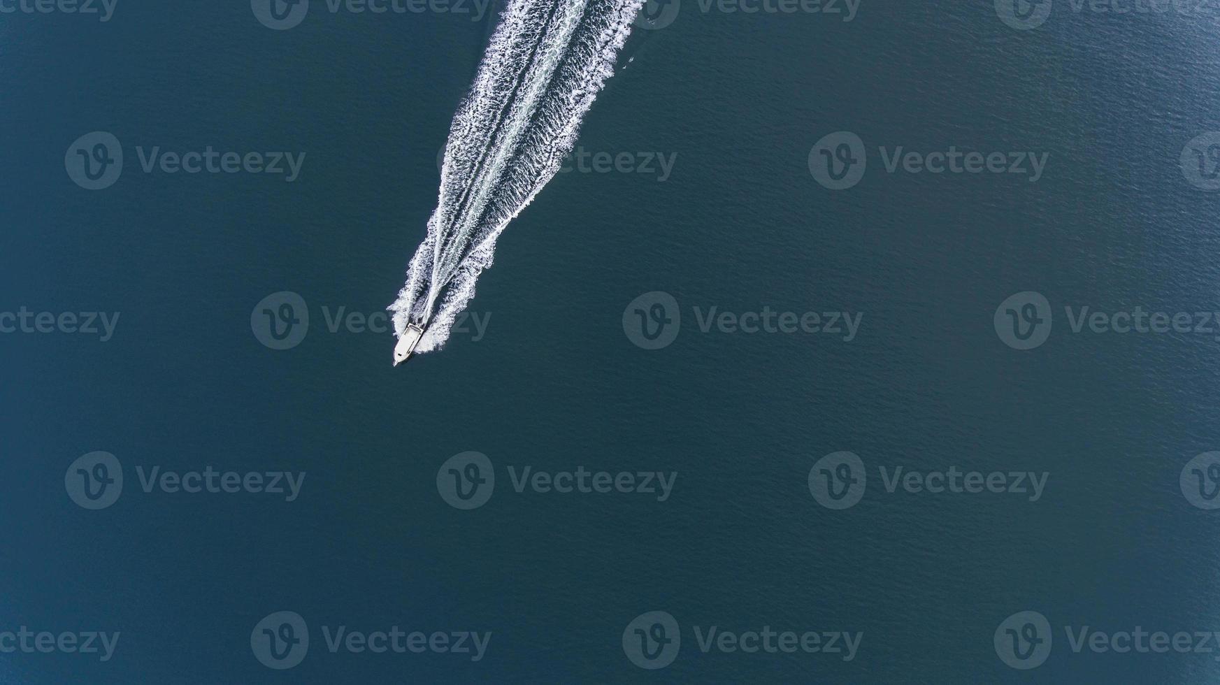 Aerial photo of small boat with white waves in wake on deep blue water