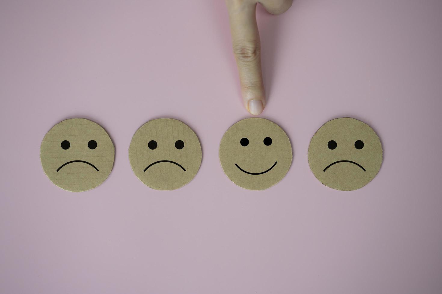 Closeup hand select happy face smile face icon paper cut on pink background photo