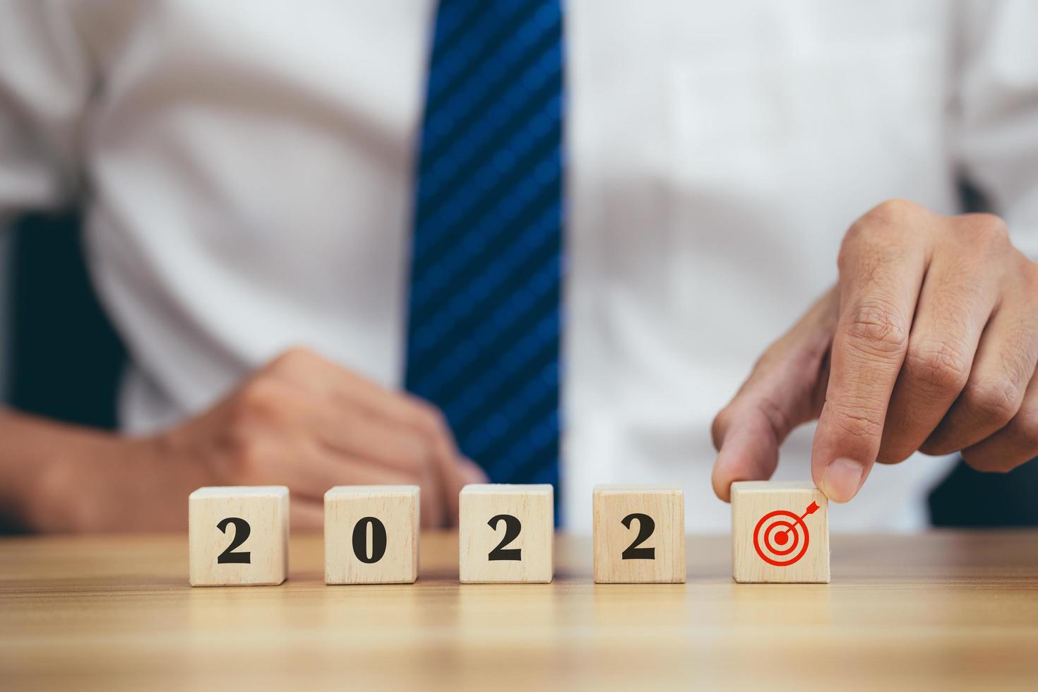 Businessman hand holding woods cube with new year icon word 2022 and goal target icon. photo