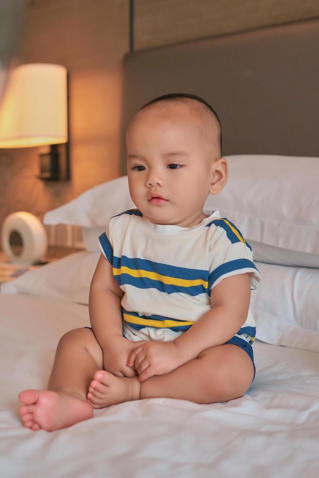 retrato de un pequeño y feliz bebé asiático de 6 meses sentado en la cama en casa foto