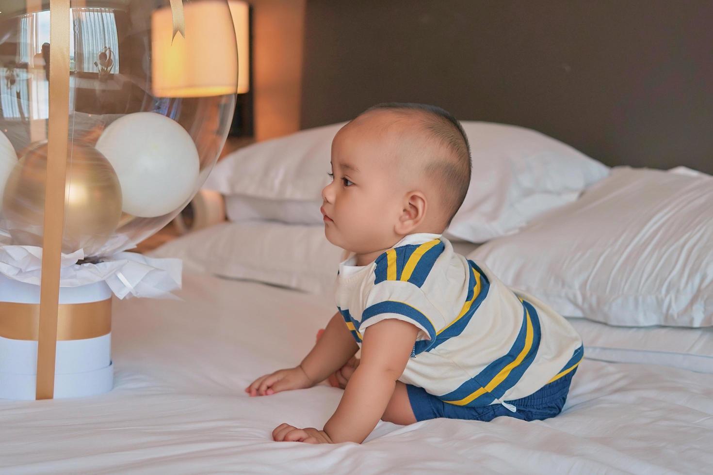 retrato de un pequeño y feliz bebé asiático de 6 meses sentado en la cama en casa foto