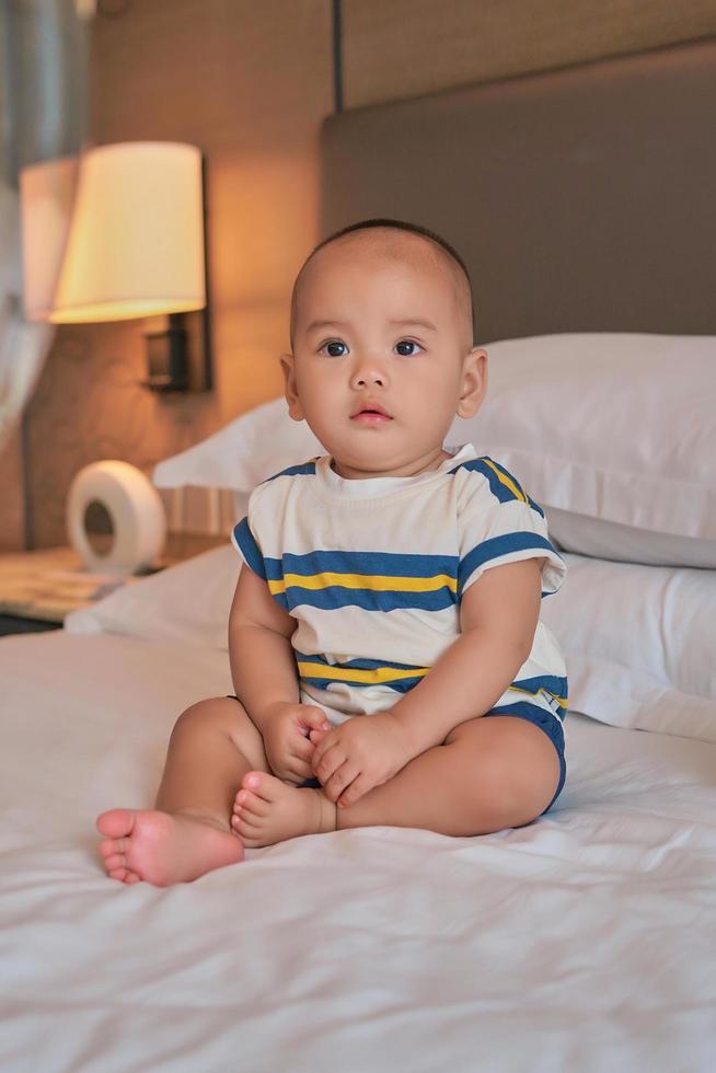 Portrait of happy little 6 month old Asian baby boy sitting on bed at home photo