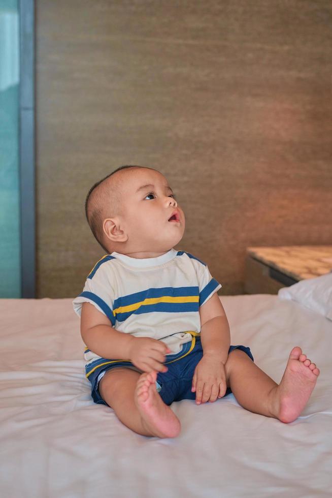 Portrait of happy little 6 month old Asian baby boy sitting on bed at home photo
