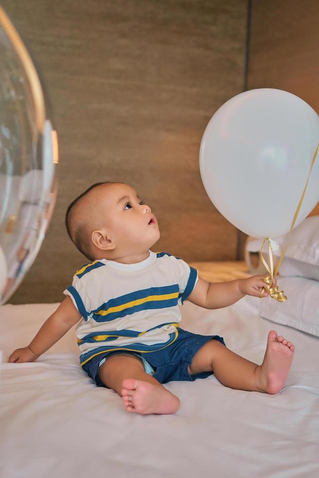 Portrait of happy 6 month old Asian baby boy sitting on bed playing photo
