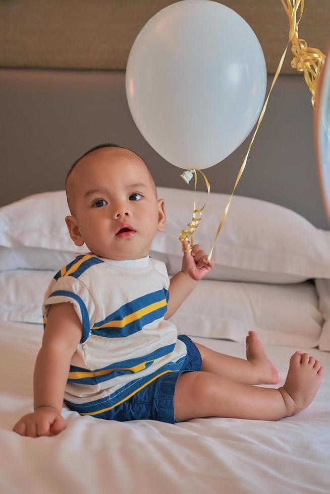 Portrait of happy 6 month old Asian baby boy sitting on bed playing photo