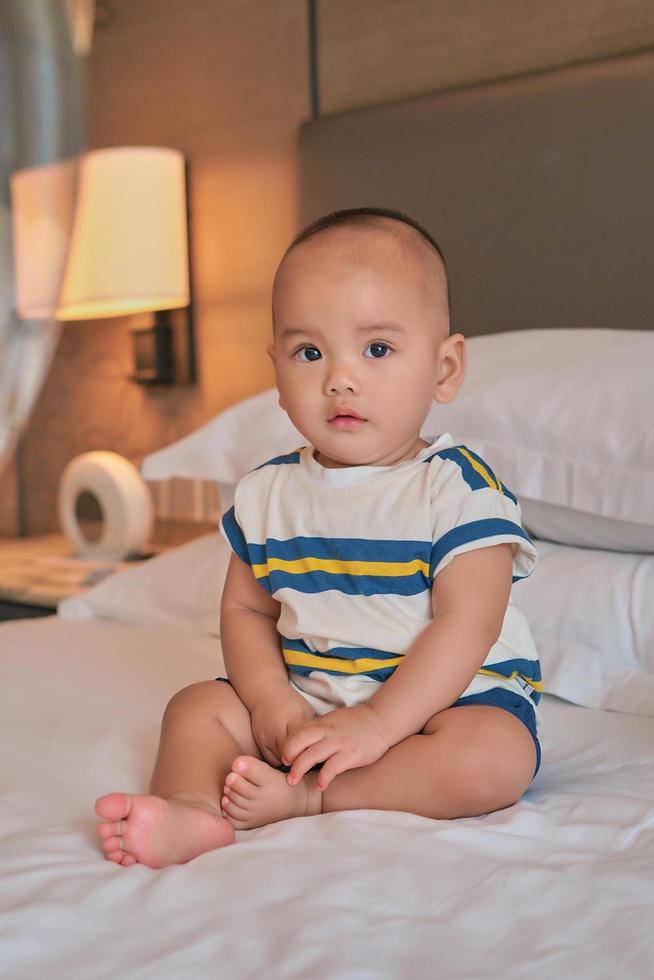 retrato de un pequeño y feliz bebé asiático de 6 meses sentado en la cama en casa foto