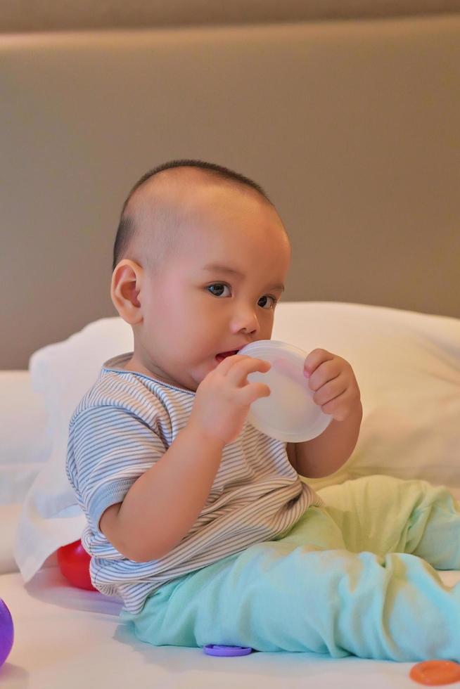 retrato de un feliz bebé asiático de 6 meses sentado en la cama jugando foto