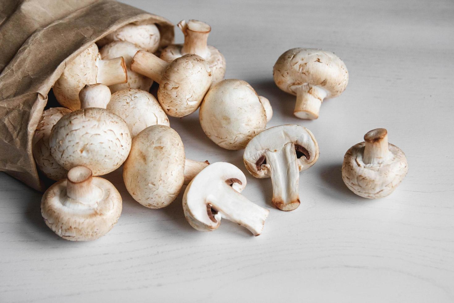 Mushrooms champignons in paper bag on a white wooden table. Place for text or advertising. Top view photo