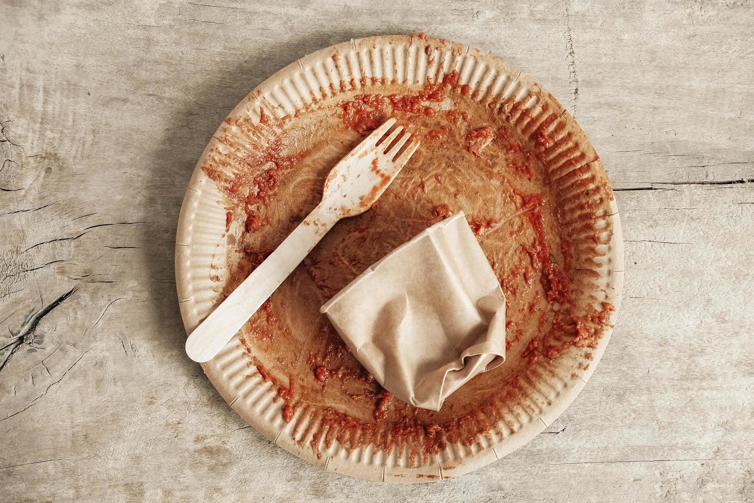 Dirty from food disposable paper utensils on a wooden background. Wooden fork and paper cup with plate on wooden background. Eco friendly disposable tableware. Top view. Copy, empty space for text photo