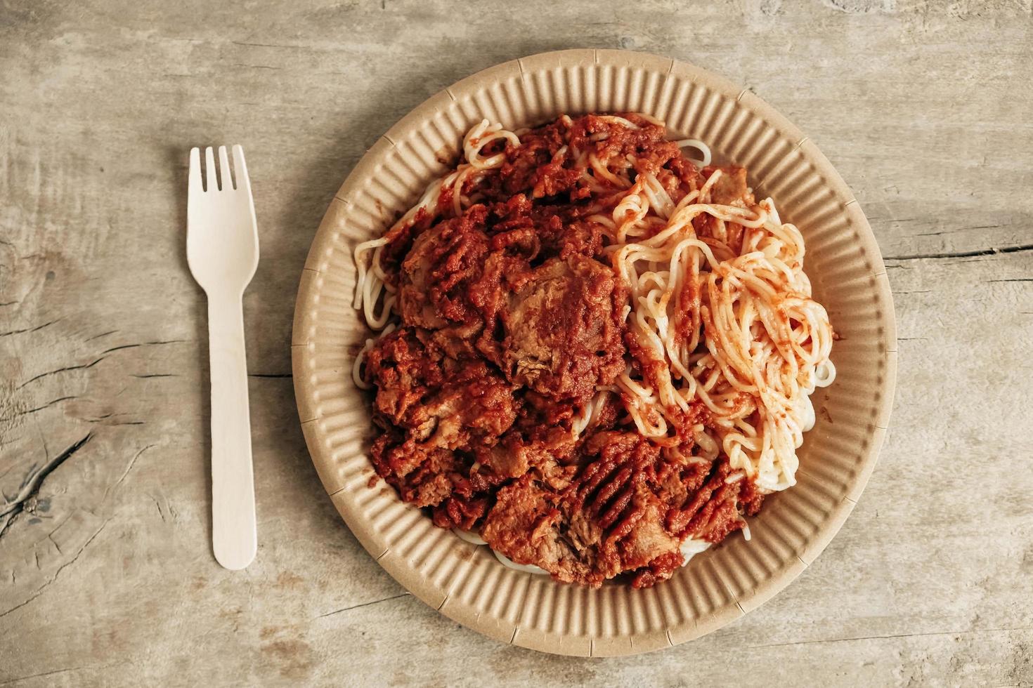 espaguetis a la boloñesa con salsa de tomate y carne picada sobre fondo rústico de madera. tenedor de madera y plato de papel. Vajilla desechable ecológica. vista superior. copiar, espacio vacío para texto foto