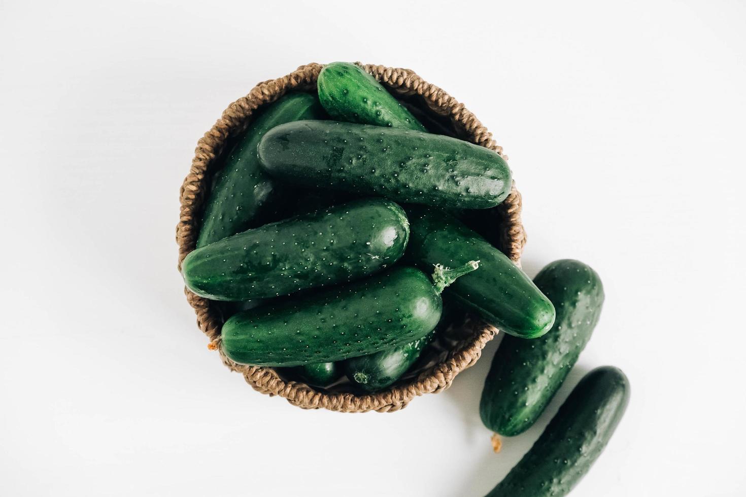 Cucumbers in a wicker basket on a white table background. Top view. Copy, empty space for text photo