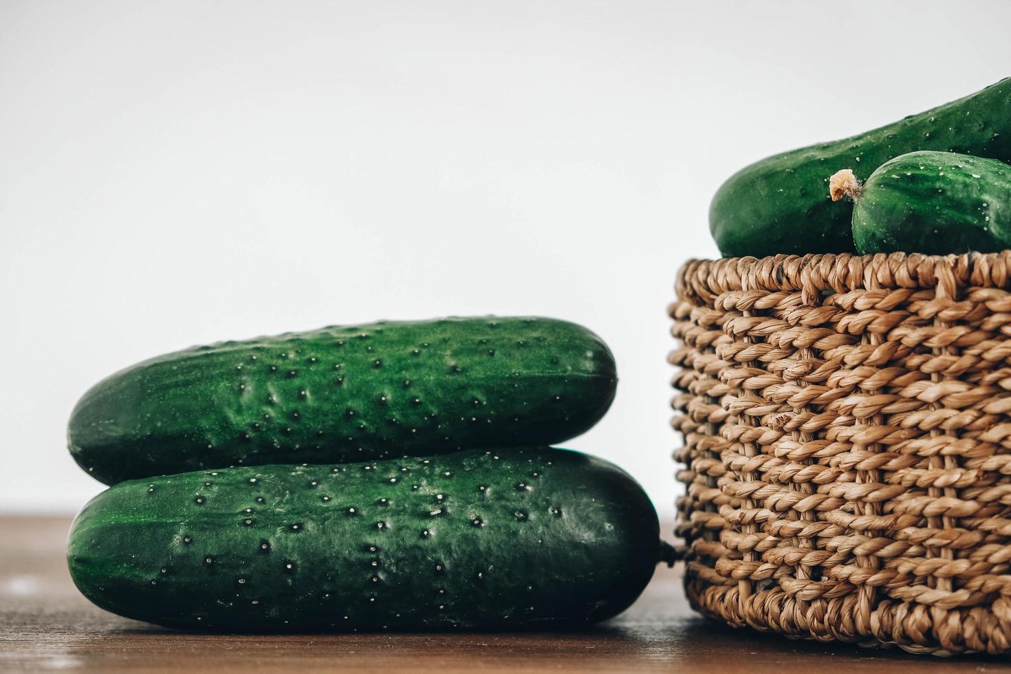 pepinos verdes frescos en una cesta de mimbre sobre un fondo de mesa de madera. copiar, espacio vacío para texto foto