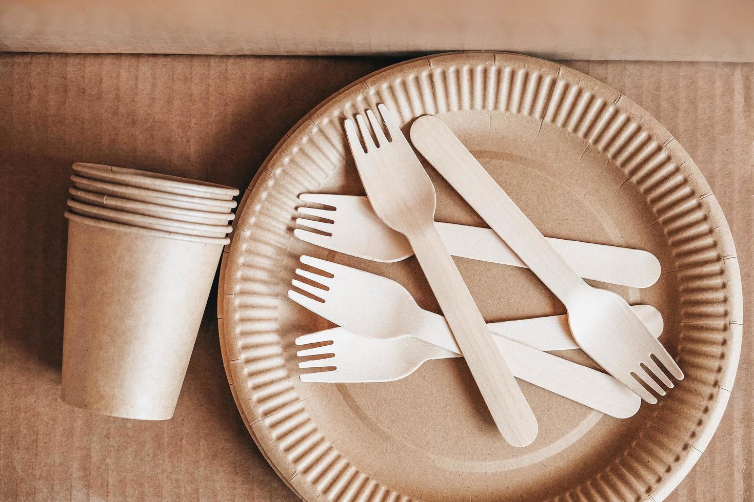 Wooden forks and paper cups with plates on kraft paper background. Eco friendly disposable tableware photo