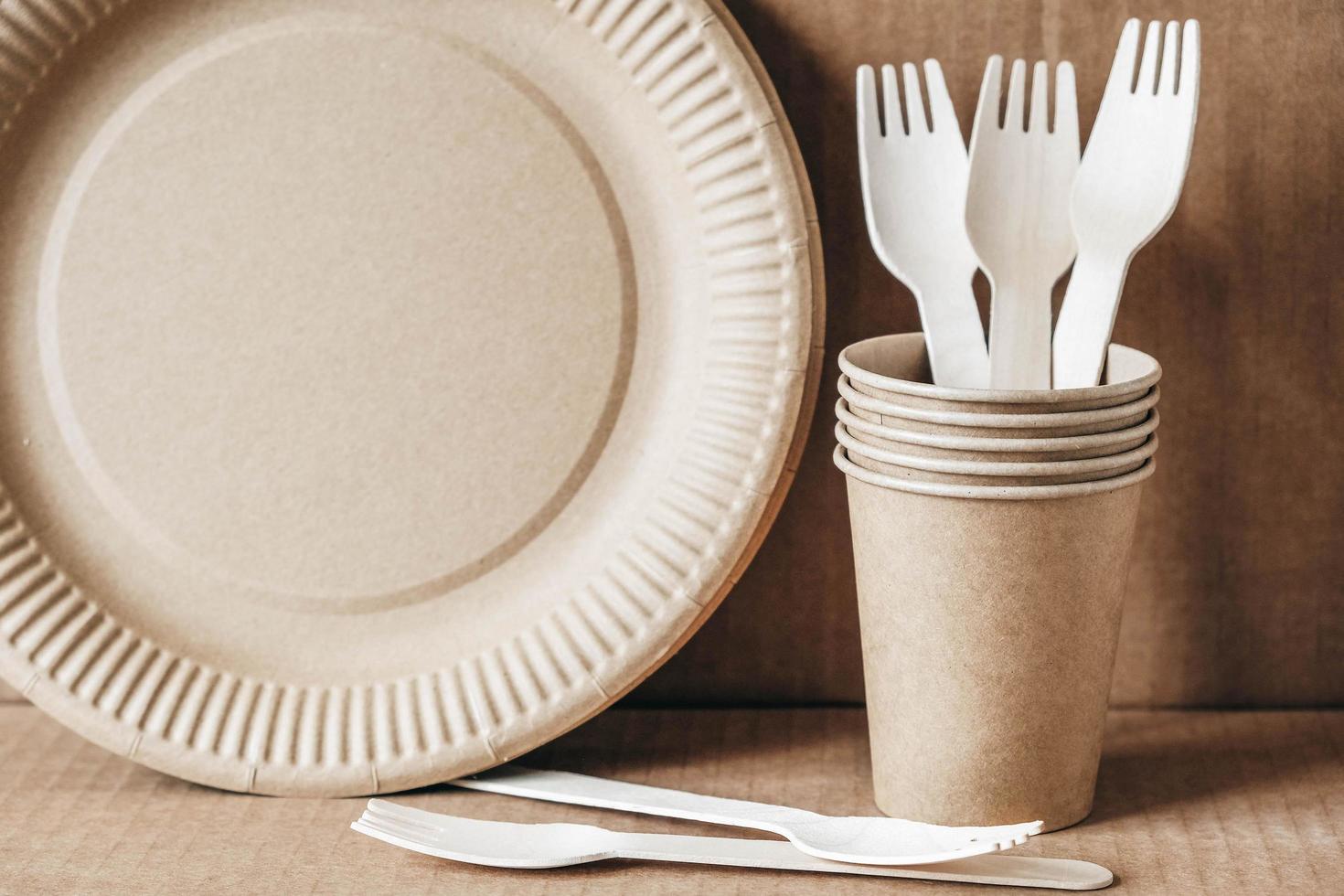 Wooden forks and paper cups with plates on kraft paper background. Eco friendly disposable tableware photo