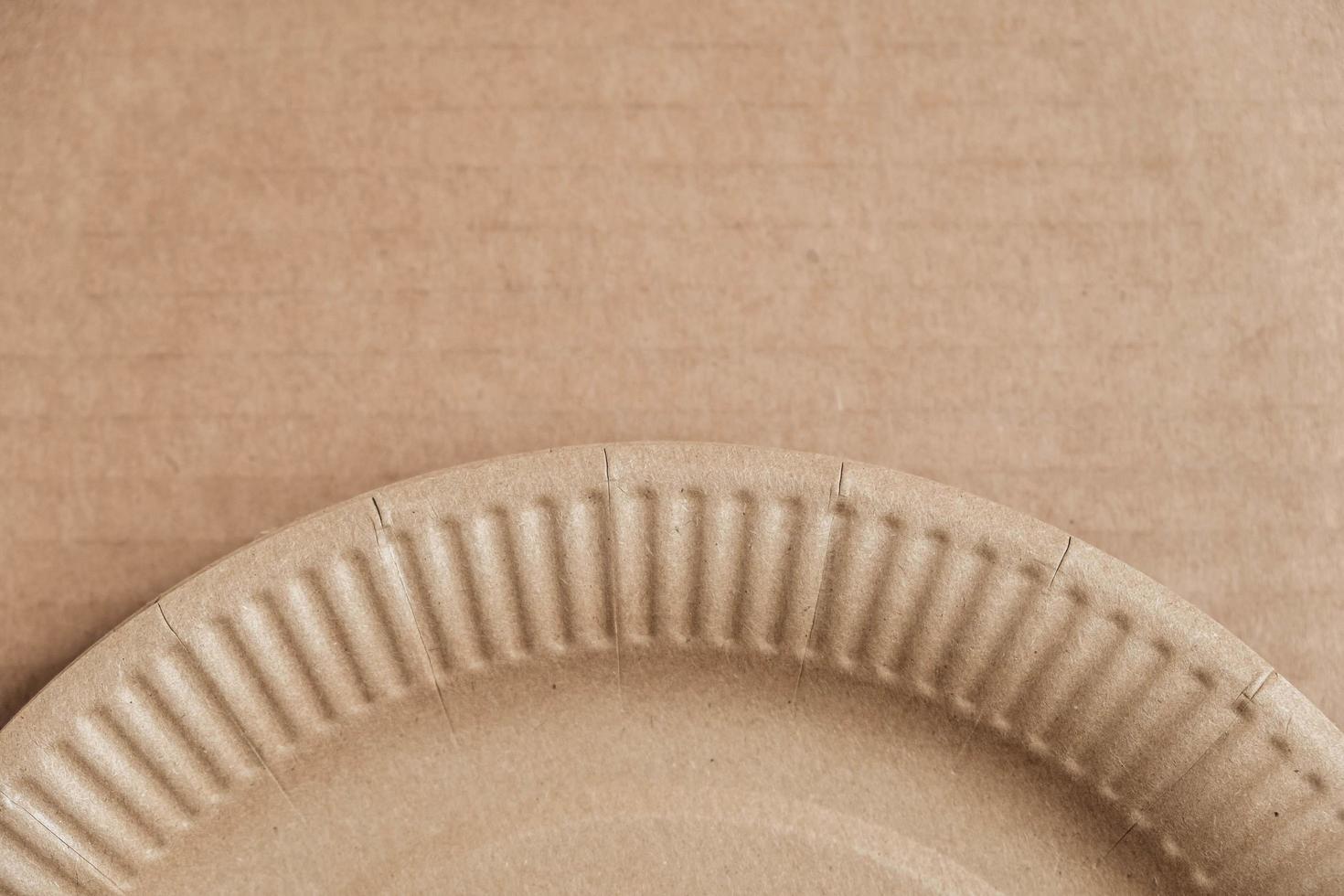 Disposable paper plate on kraft paper background. Eco friendly disposable tableware. Top view. Copy, empty space for text photo
