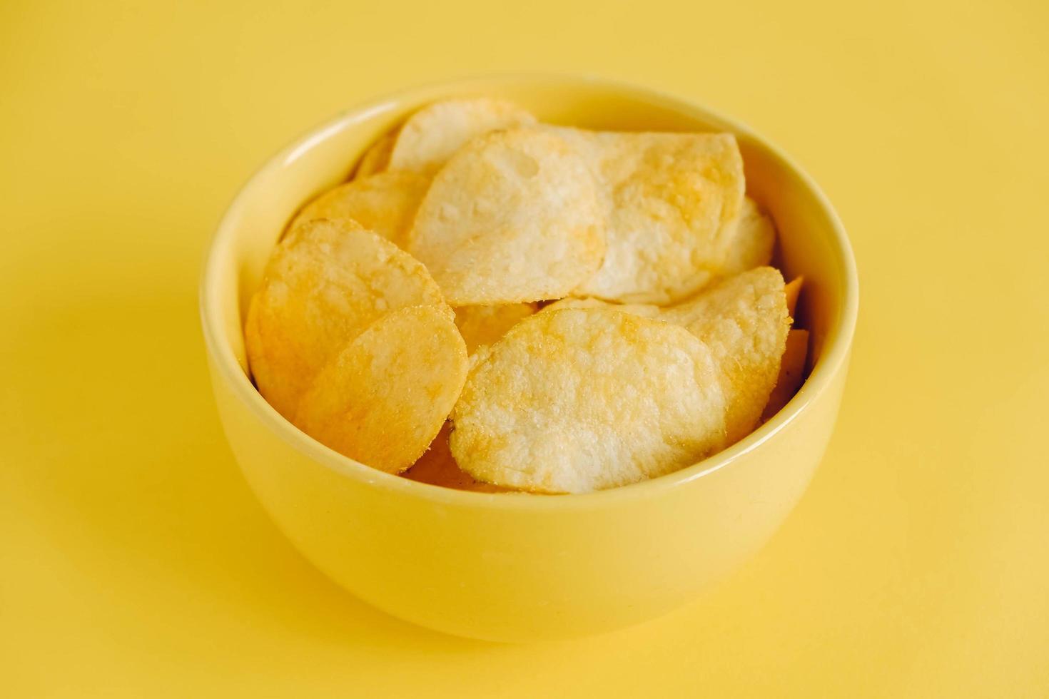 Potato chips in a yellow bowl on a yellow background photo