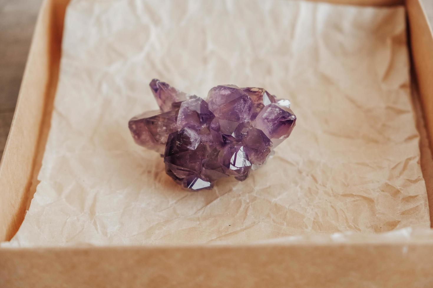 Violet amethyst crystal in a kraft paper box on wooden background photo