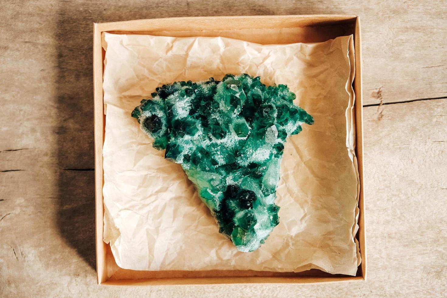 Esmeralda cruda y cristal de roca en bruto de piedras preciosas en una caja de papel kraft sobre fondo de madera foto